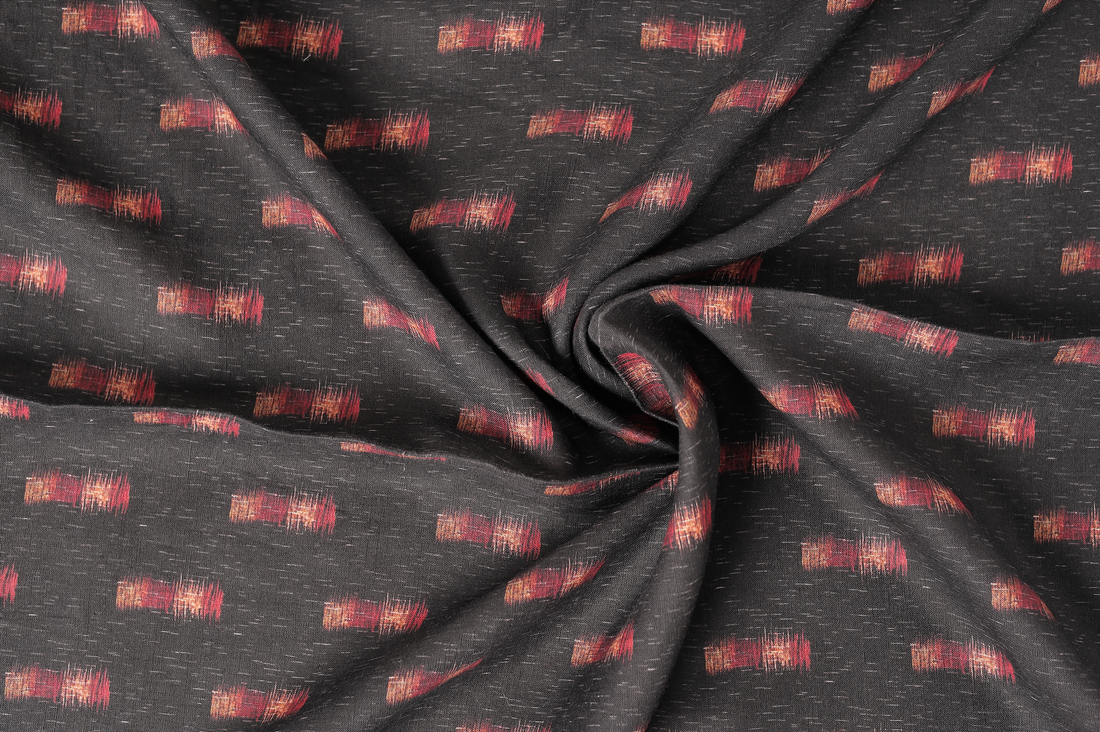 Close-up of a dark charcoal fabric twisted in a spiral fold, featuring small scattered red and orange woven motifs with a subtle textured weave visible across the surface.