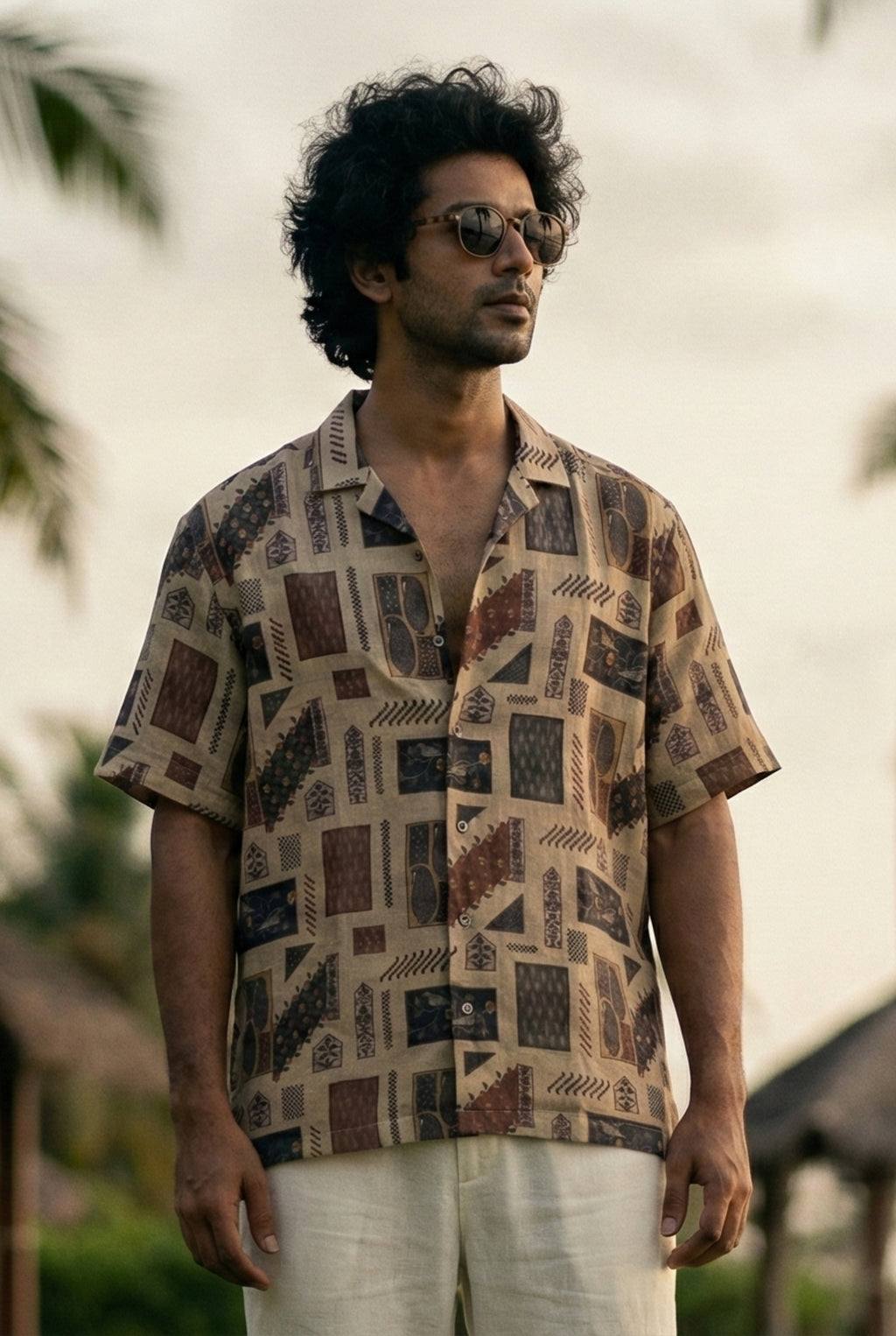 Man wearing a premium geometric print short-sleeve shirt with a relaxed tailored fit, styled outdoors in soft natural light, highlighting breathable fabric, fluid drape, and contemporary summer menswear.