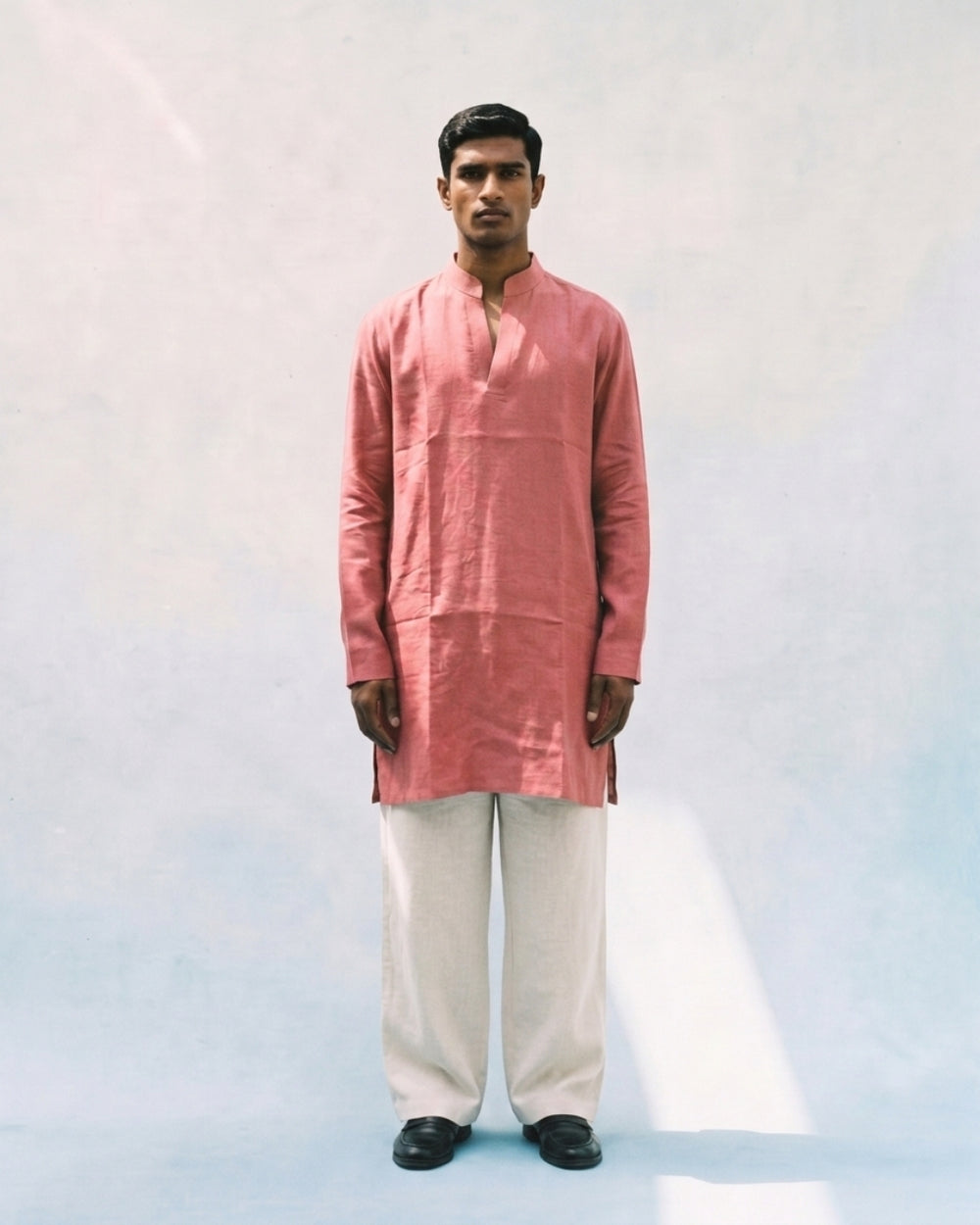 Coral pink linen kurta with a band collar, long sleeves, short button placket, side slits, and a relaxed straight fit, paired with white trousers.