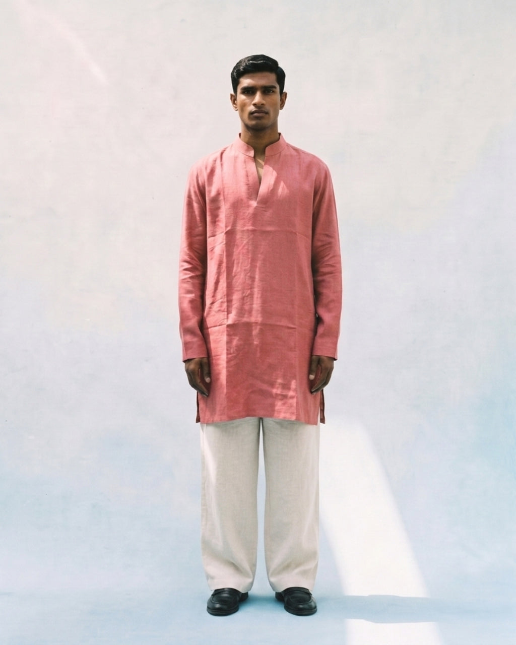 Coral pink linen kurta with a band collar, long sleeves, short button placket, side slits, and a relaxed straight fit, paired with white trousers.