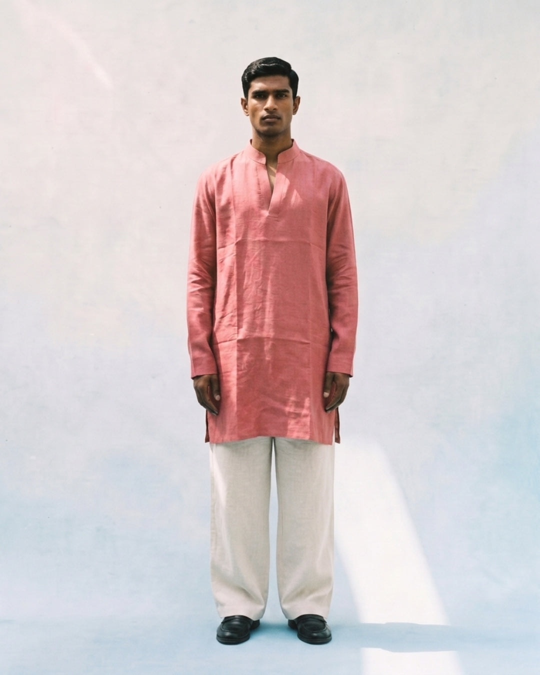 Coral pink linen kurta with a band collar, long sleeves, short button placket, side slits, and a relaxed straight fit, paired with white trousers.
