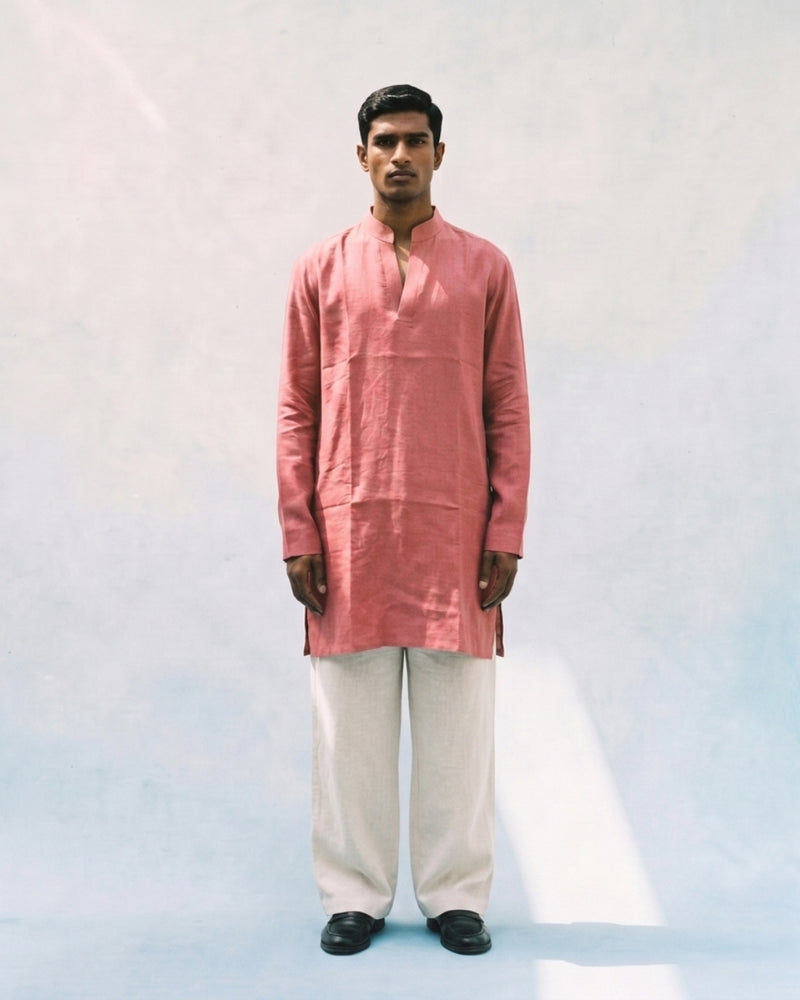 Coral pink linen kurta with a band collar, long sleeves, short button placket, side slits, and a relaxed straight fit, paired with white trousers.