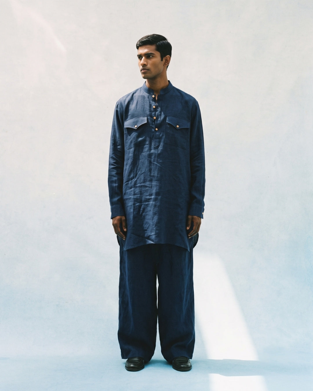 Navy blue linen kurta with a band collar, long sleeves, buttoned half-placket, and two flap chest pockets, featuring a relaxed straight fit and paired with matching wide-leg linen trousers.