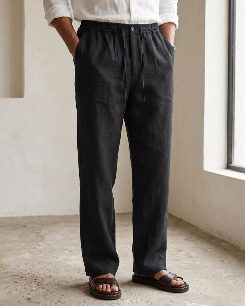 Black linen trousers with an elasticated waistband, front button closure, adjustable drawstring, side pockets, and a relaxed straight-leg fit.