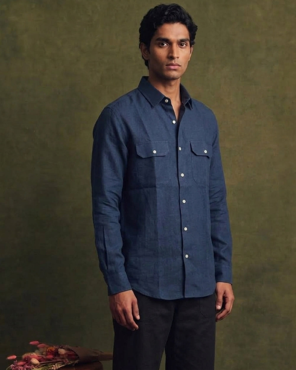 Navy blue linen shirt with a classic collar, full button-front closure, long sleeves, and two flap chest pockets, styled with black trousers.