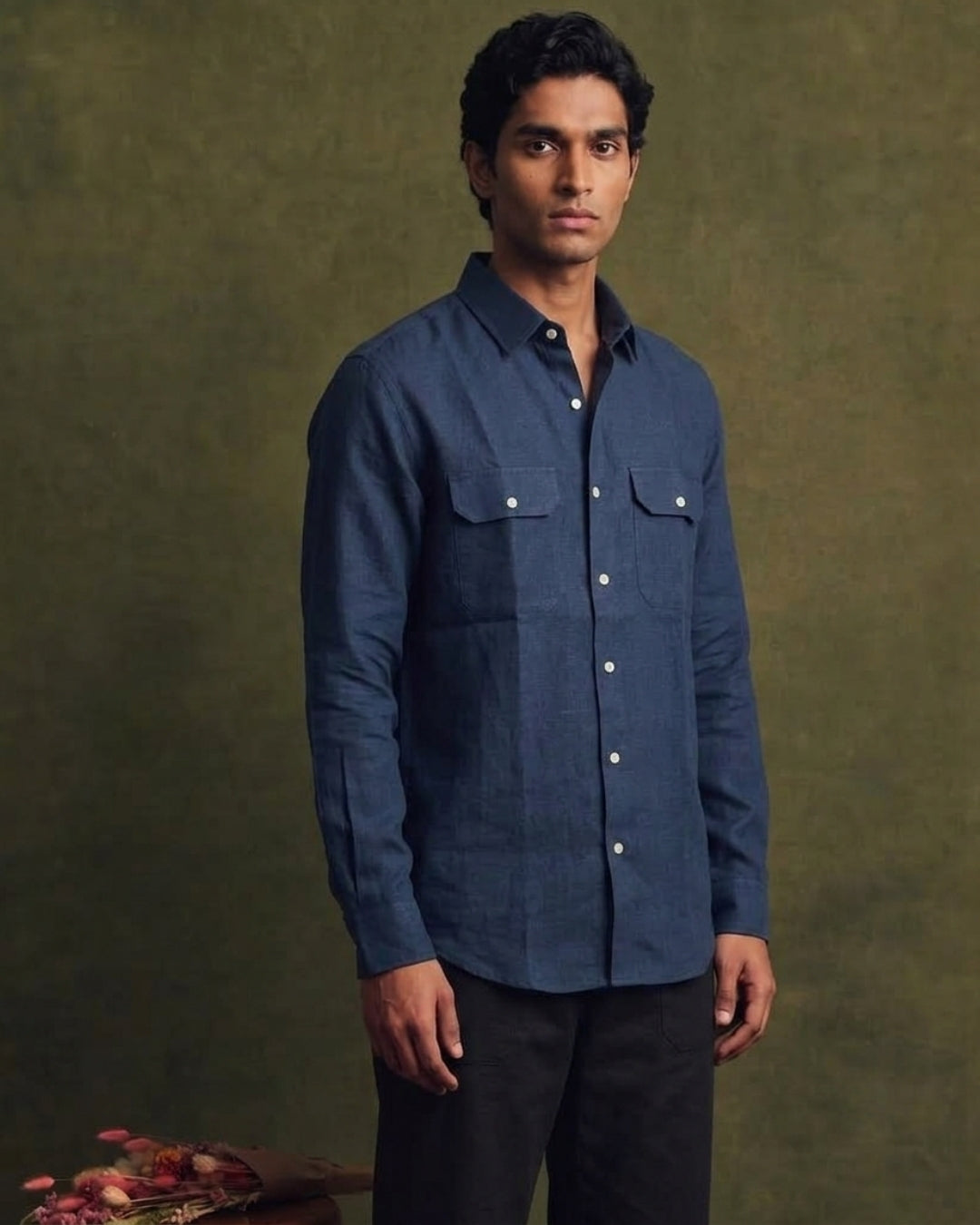 Navy blue linen shirt with a classic collar, full button-front closure, long sleeves, and two flap chest pockets, styled with black trousers.