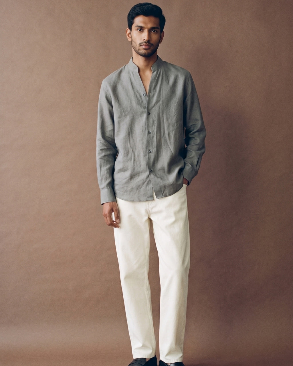 Sage grey linen shirt with a band collar, full button-front closure, long sleeves, and a relaxed fit, paired with white trousers.