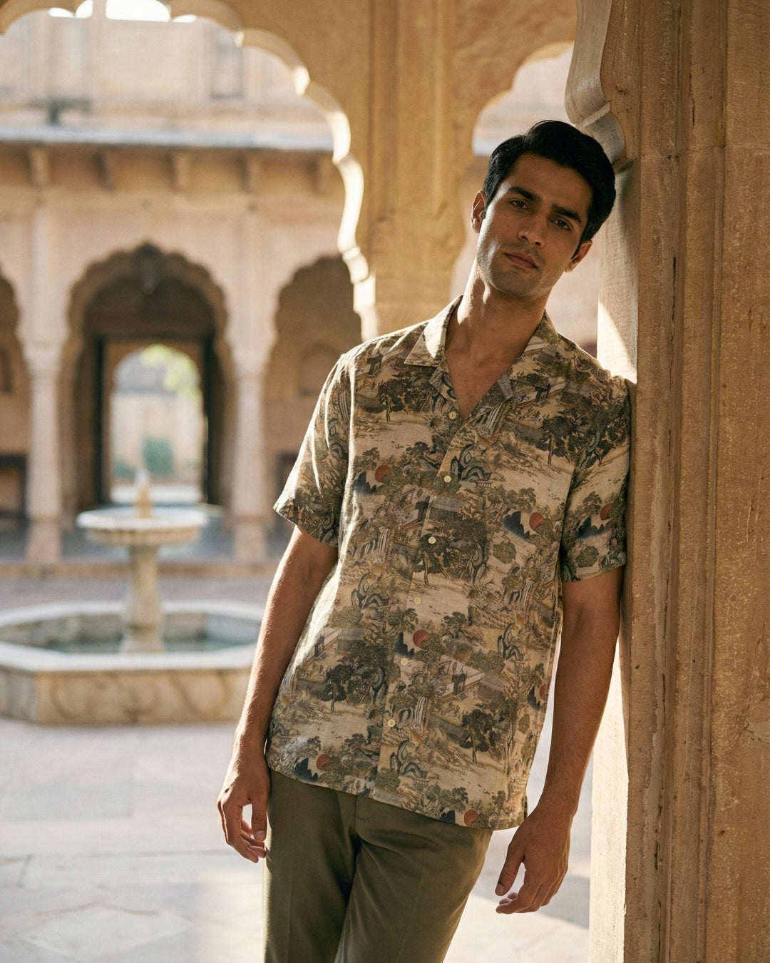 Man wearing a printed linen shirt standing in an outdoor setting with arches and a fountain.