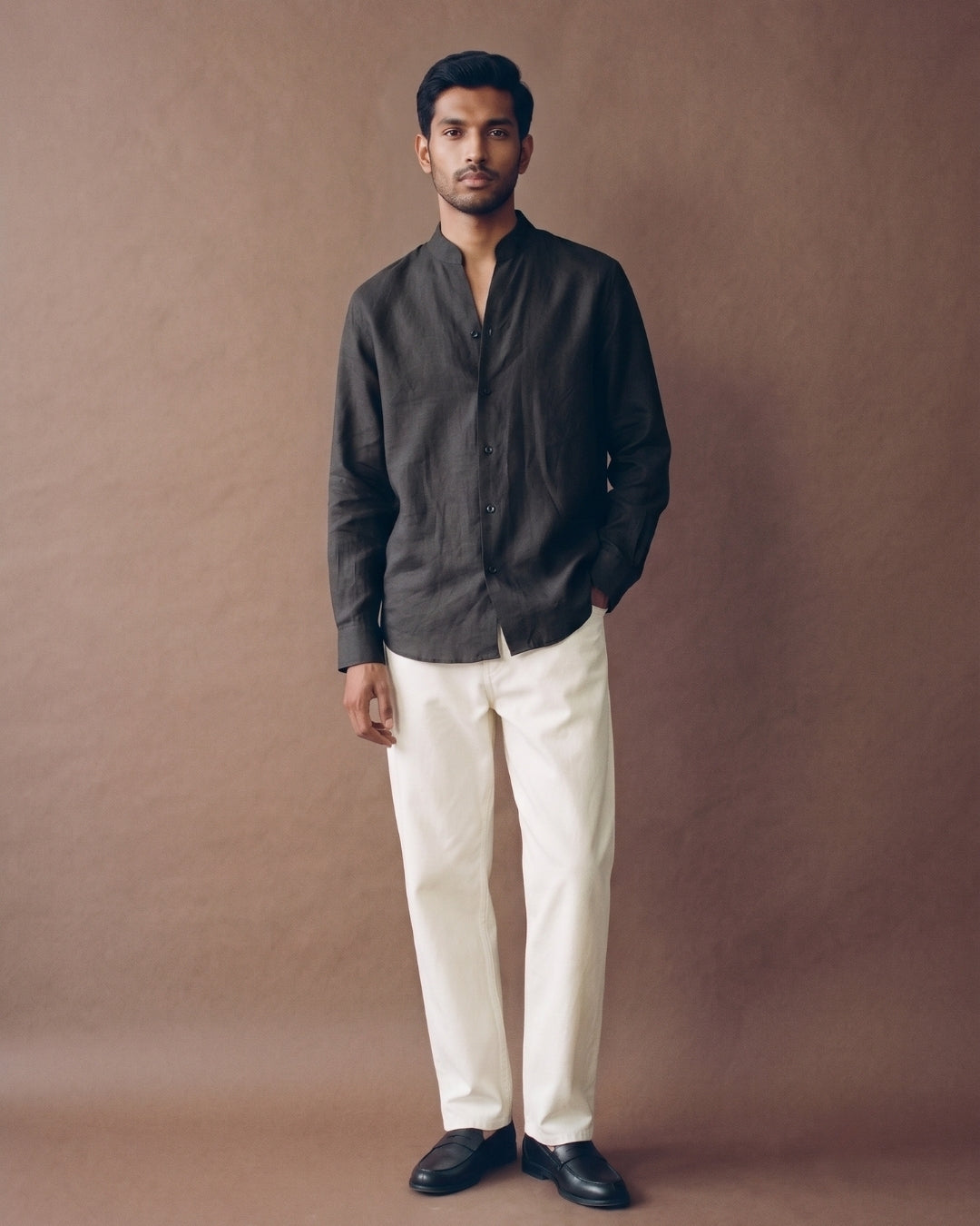  Charcoal black linen shirt with a band collar, full button-front closure, long sleeves, and a relaxed fit, paired with white trousers.