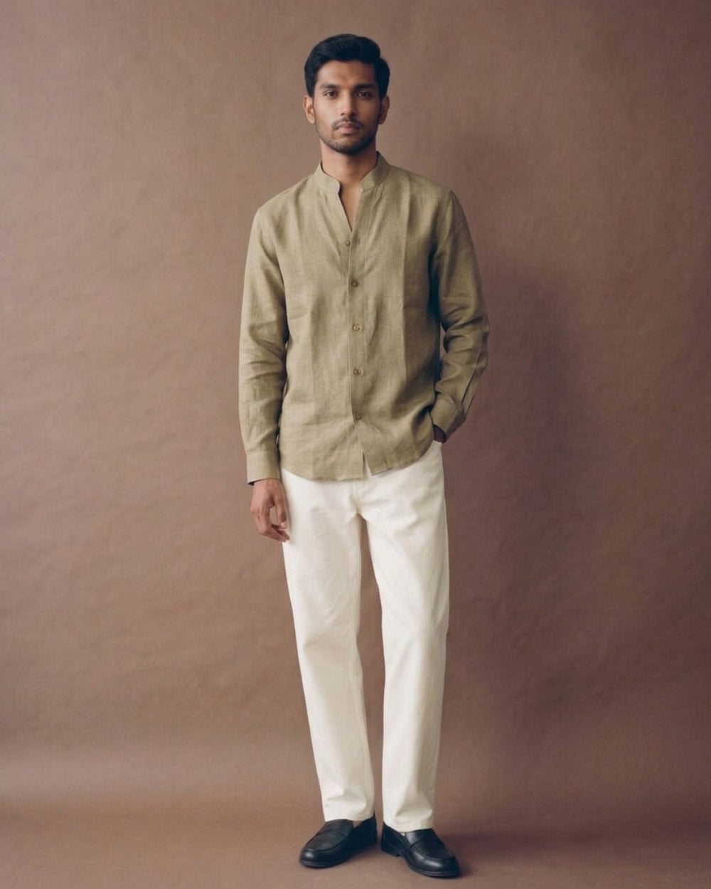 Golden beige linen shirt with a band collar, full button-front closure, long sleeves, and a relaxed fit, paired with white trousers.