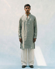 Sage green linen kurta with a band collar, long sleeves, short button placket, side slits, and a relaxed straight fit, paired with white trousers.