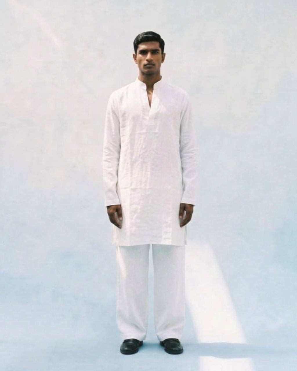  White linen kurta with a band collar, long sleeves, straight relaxed fit, and a short buttoned placket, paired with matching white trousers.