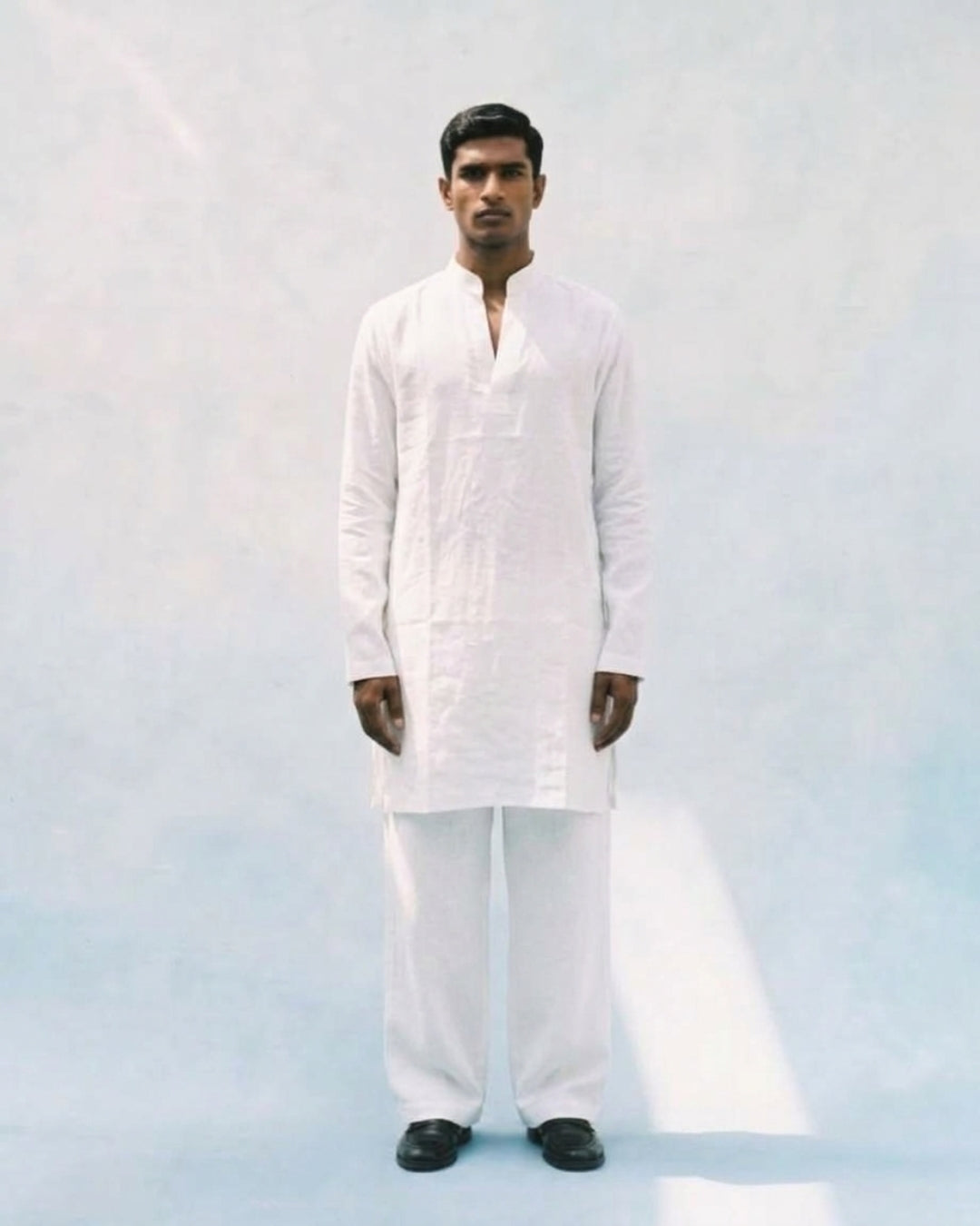 White linen kurta with a band collar, long sleeves, straight relaxed fit, and a short buttoned placket, paired with matching white trousers.