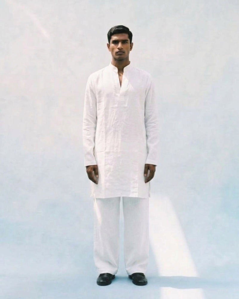  White linen kurta with a band collar, long sleeves, straight relaxed fit, and a short buttoned placket, paired with matching white trousers.