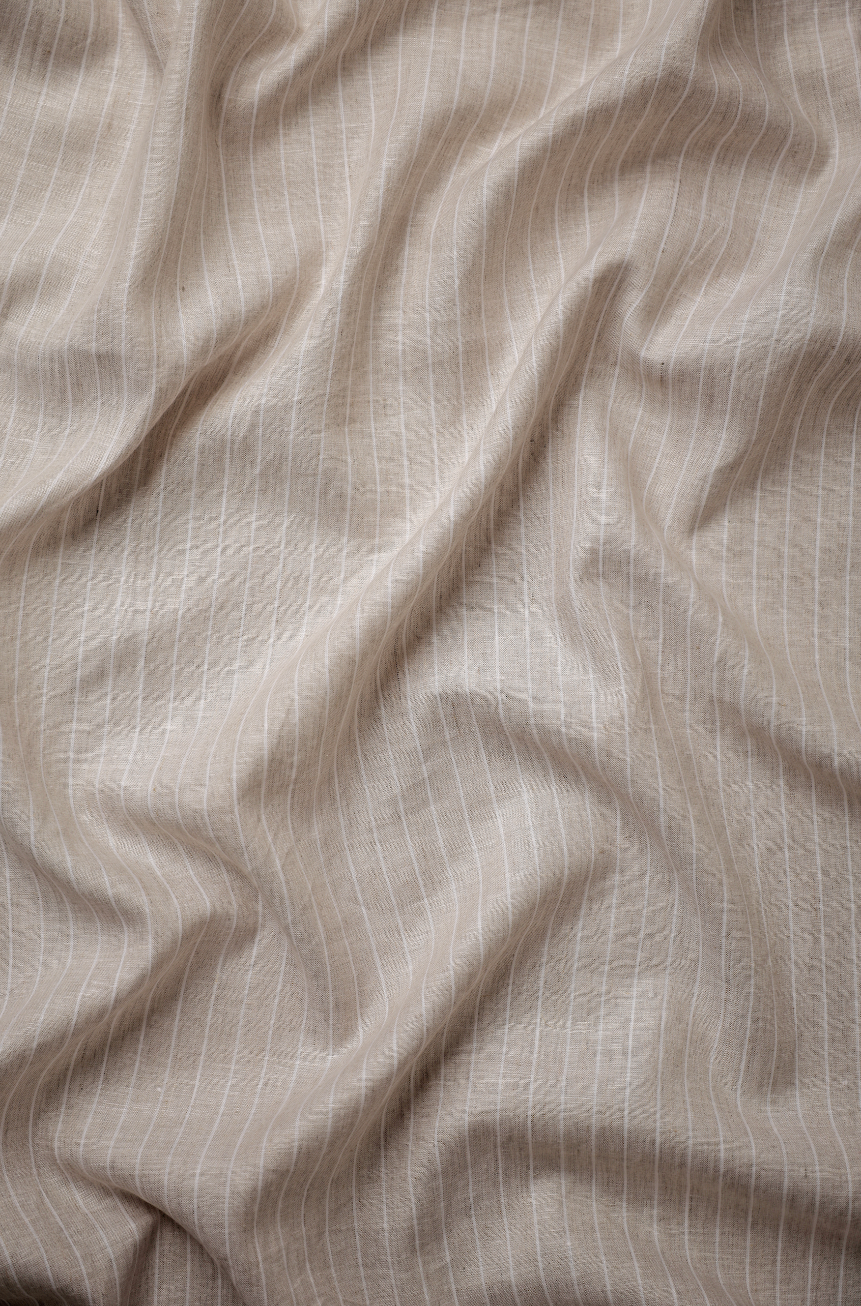 Natural beige linen fabric with subtle horizontal stripes, highlighting a relaxed weave, soft creasing, and understated textured finish.