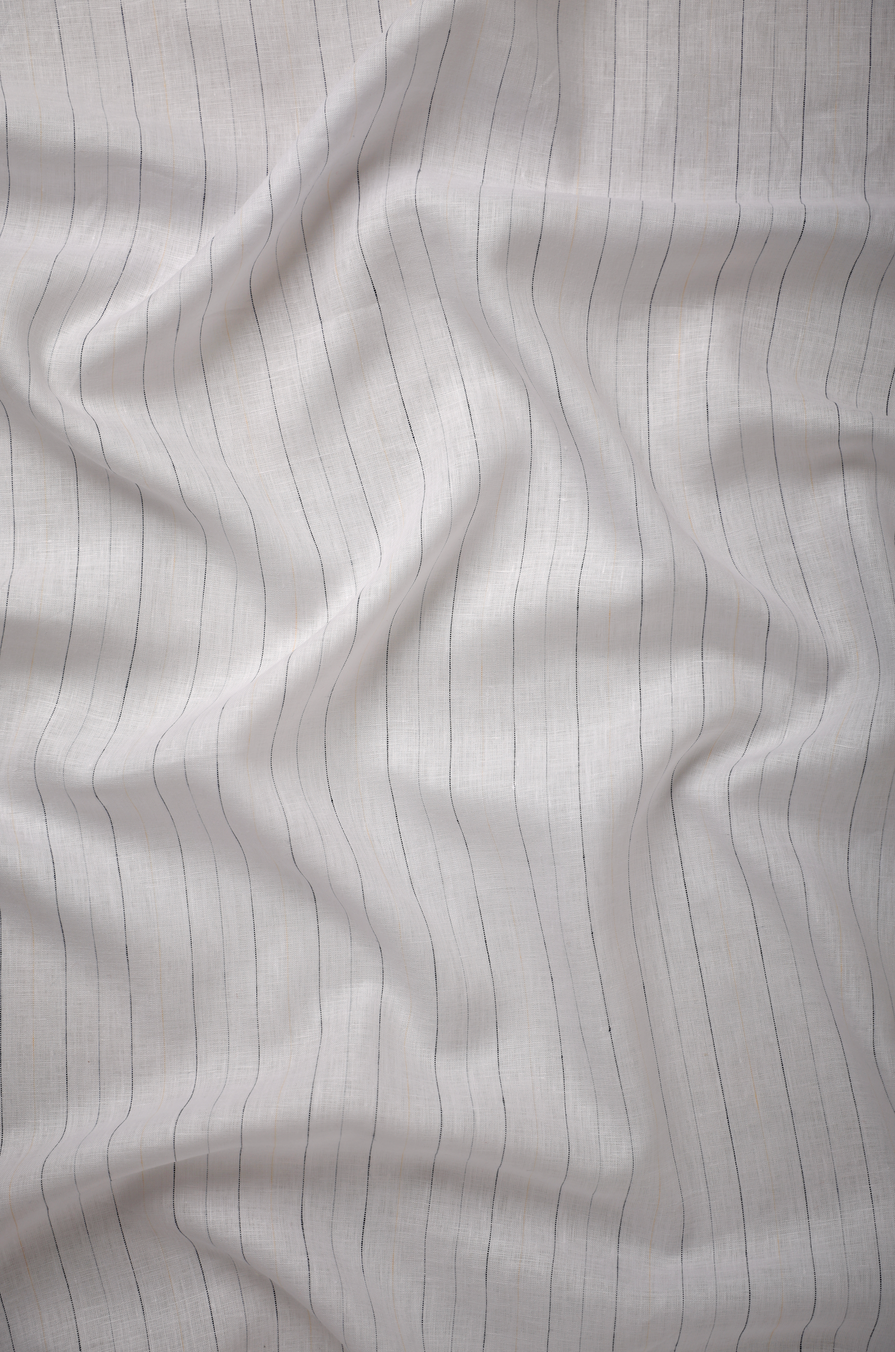 Off-white linen fabric with fine black pinstripes, displaying a clean linear pattern, fluid drape, and refined woven texture.