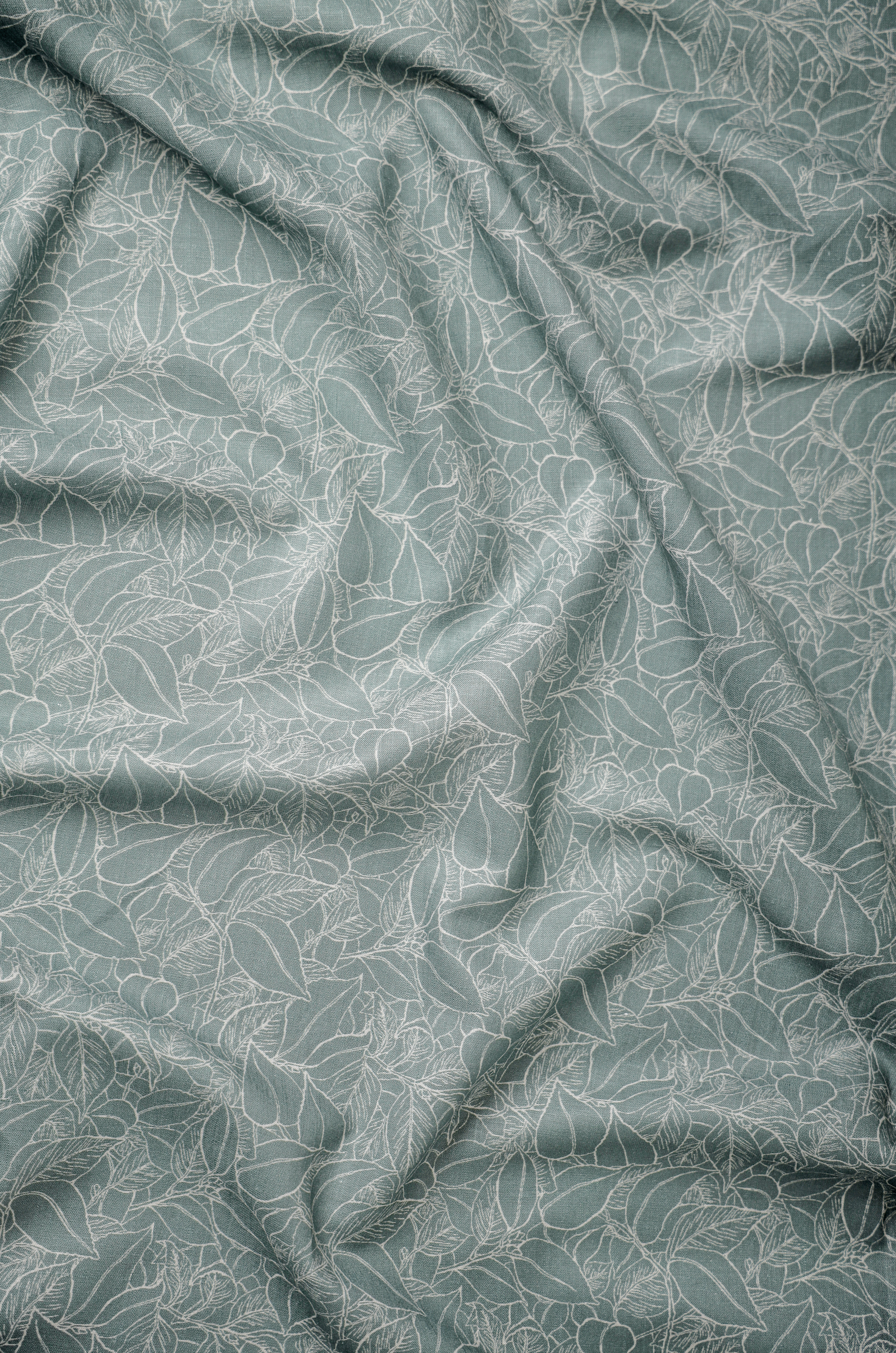Muted green linen fabric with fine botanical linework, showcasing detailed surface design, breathable weave, and elegant natural movement.