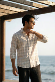 Man on a porch adjusting his collar while watching the ocean, wearing the Drift Check pure linen shirt by Tyra