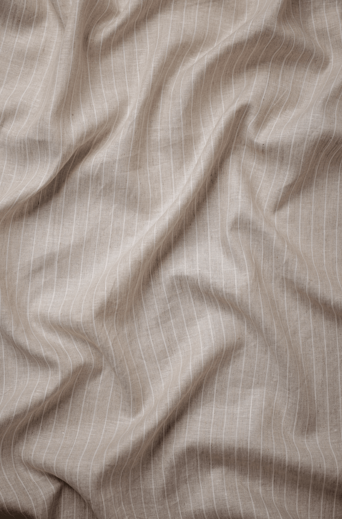 Flat lay of Haze-Lēkhā 60 lea pure linen fabric in taupe with fine white pinstripes. Sold by the metre by Tyra