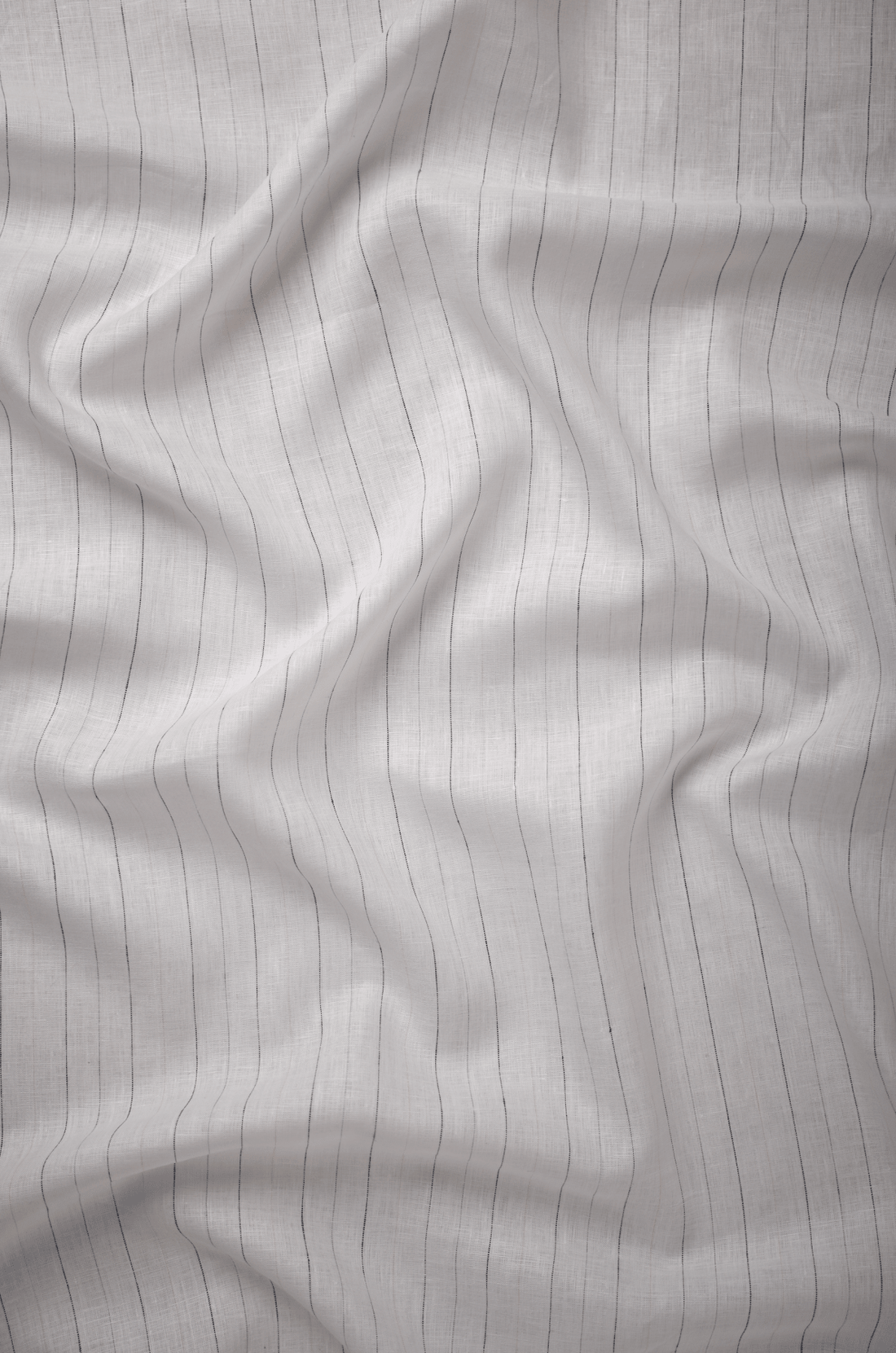 Flat lay of Kārsha 60 lea pure linen fabric in pale white with fine dark pinstripes. Sold by the metre by Tyra