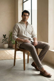 Man seated on a chair looking straight at the camera, wearing the Mitti beige pure linen shirt by Tyra
