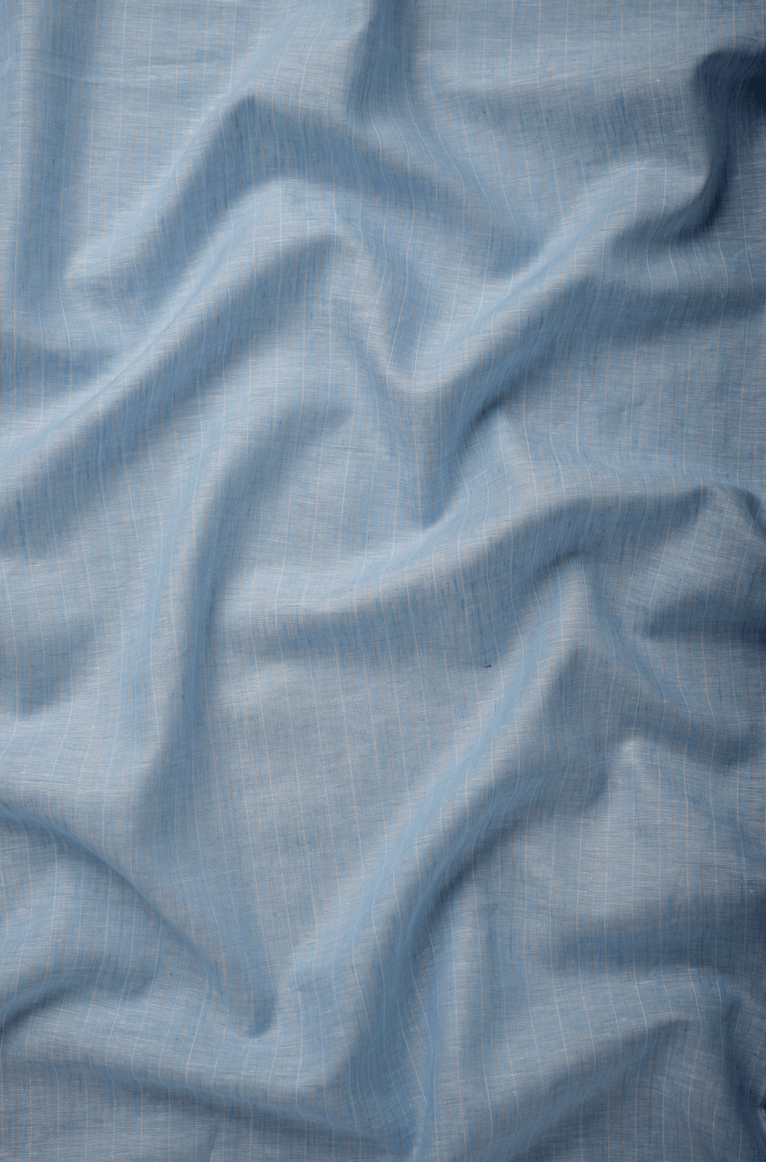 Flat lay of Nabh 60 lea pure linen fabric in chambray blue, showing the weave. Sold by the metre by Tyra